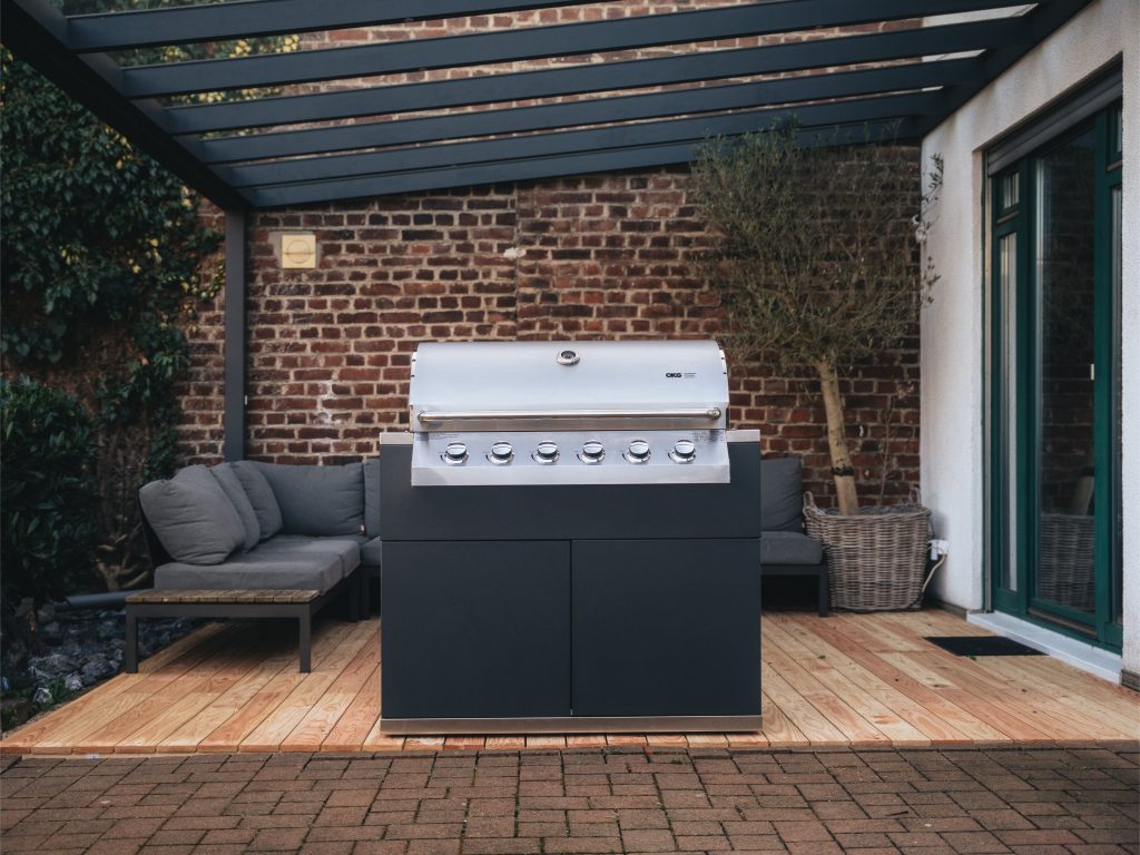 Ein großer Gasgrill steht auf einer überdachten Terrasse vor einer Backsteinwand