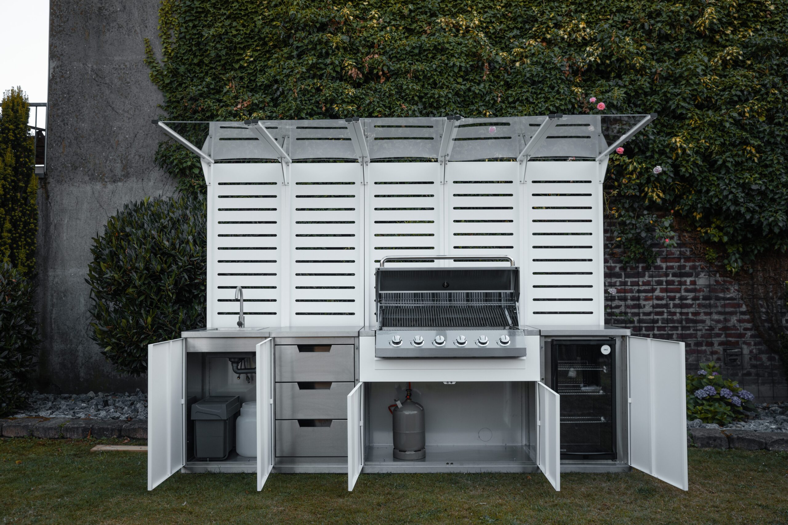 Eine moderne Außenküche mit Grill steht vor einer bewachsenen Gartenwand